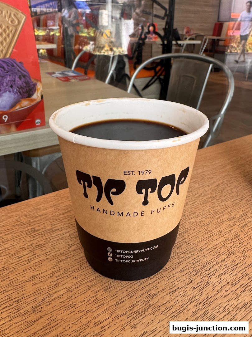 A cup of coffee from Tip Top Curry Puff with their branding visible.