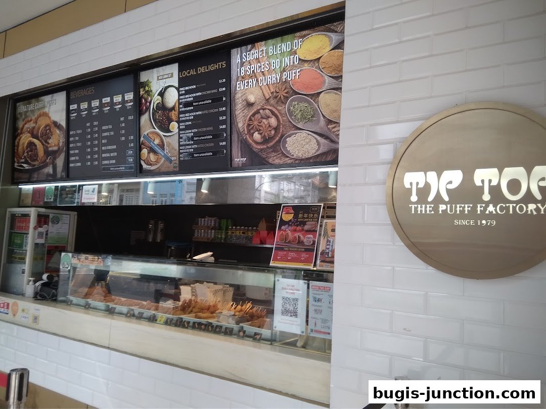 A display of curry puffs, beverages, and local delights with prices at Tip Top Curry Puff.
