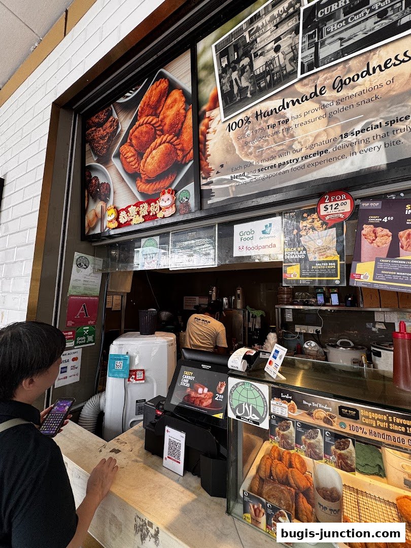 A customer orders at the counter of Tip Top Curry Puff, showcasing their popular snacks.