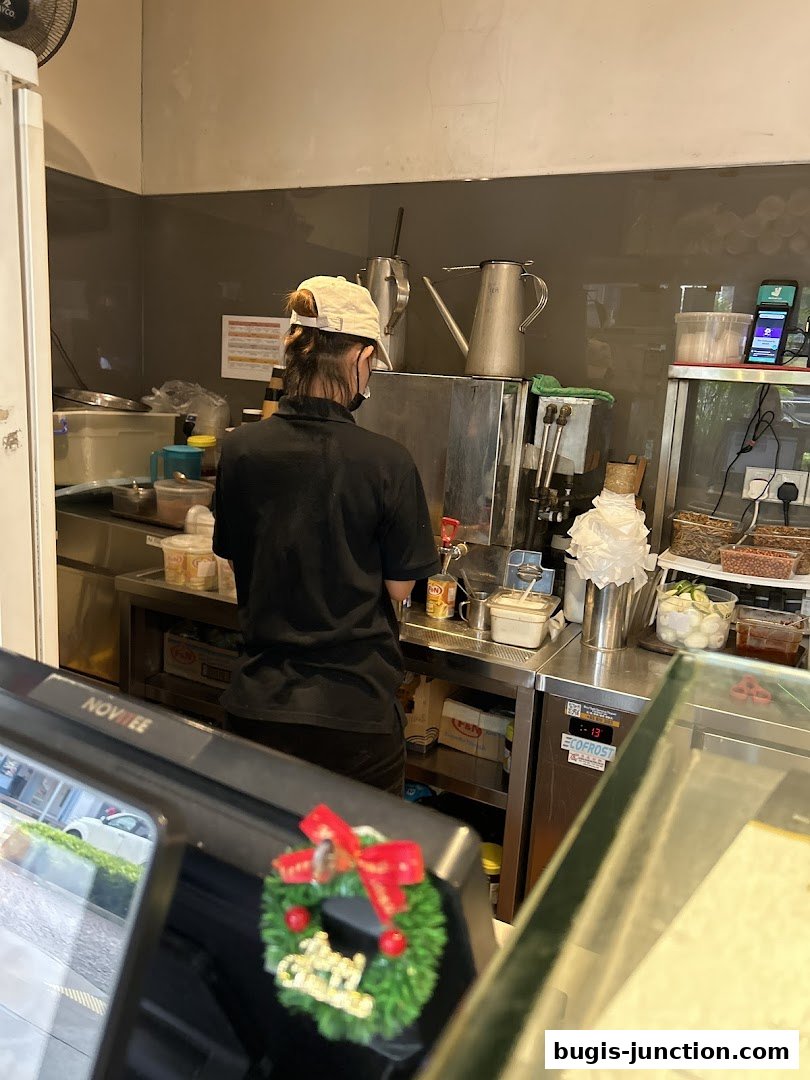 A staff member works behind the counter at Tip Top Curry Puff, with kitchen equipment visible.