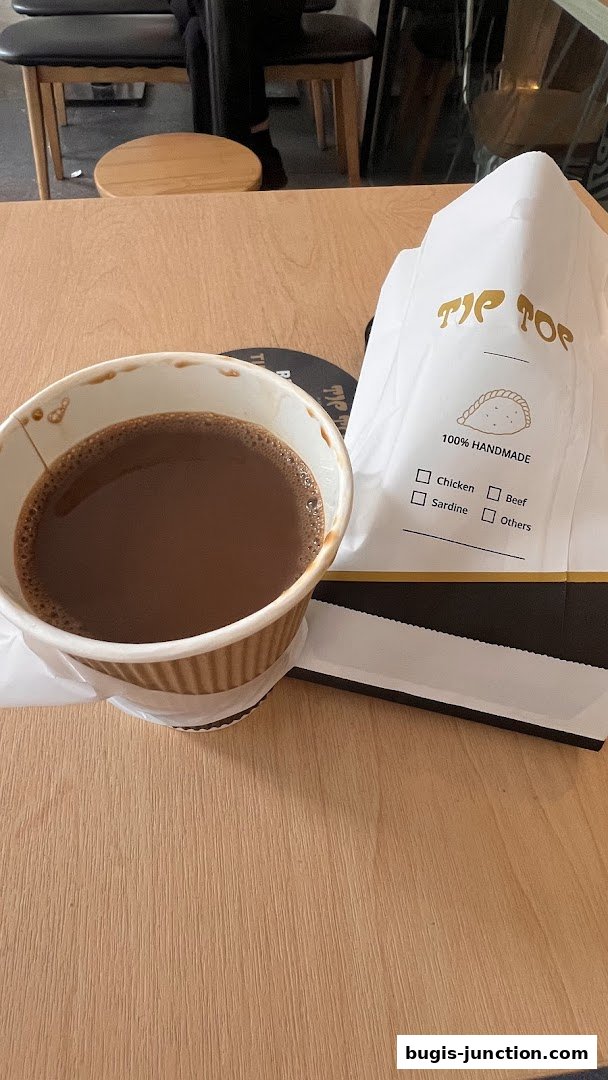 A cup of coffee and a bag from Tip Top Curry Puff on a wooden table.