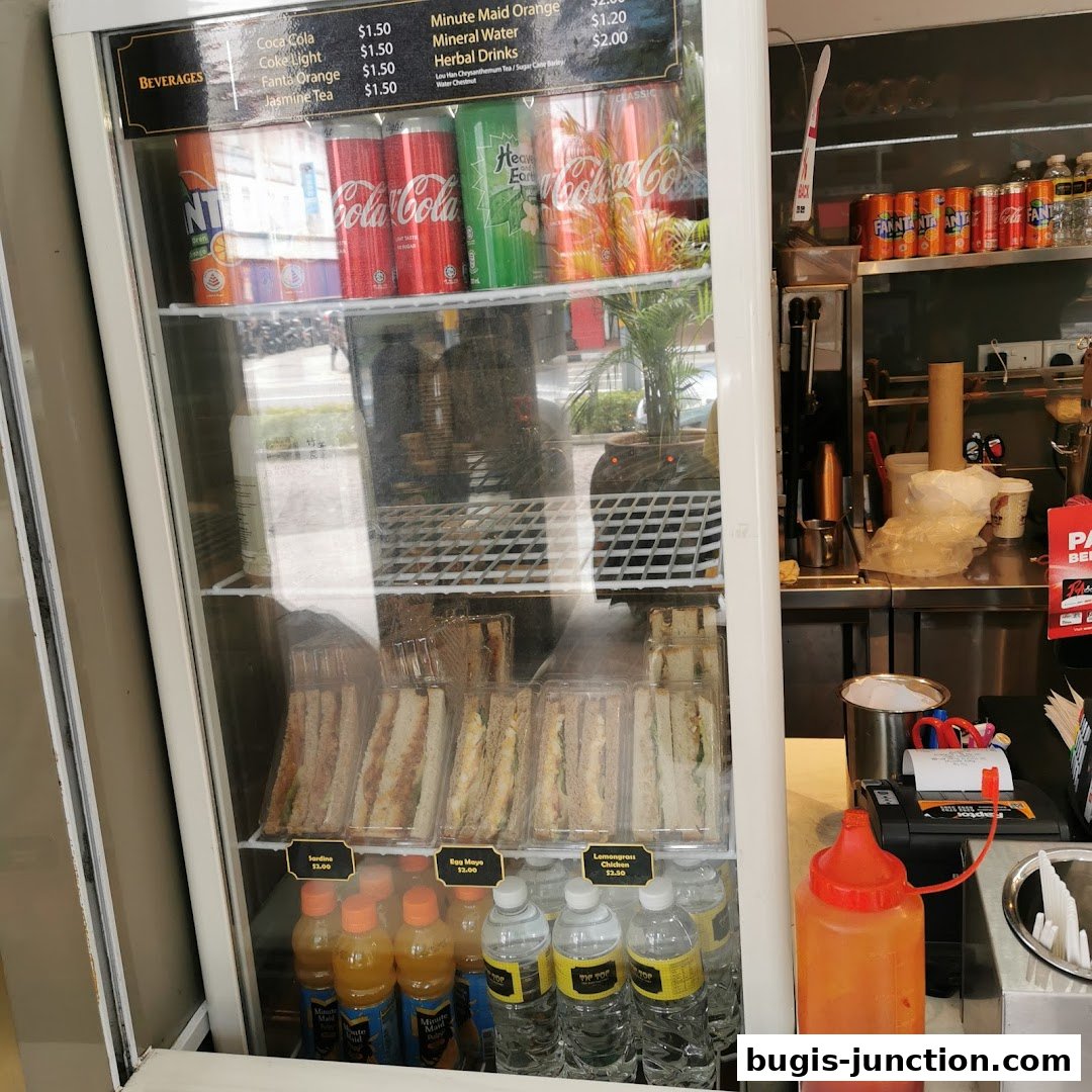 A display fridge filled with beverages and sandwiches, with a price list visible.