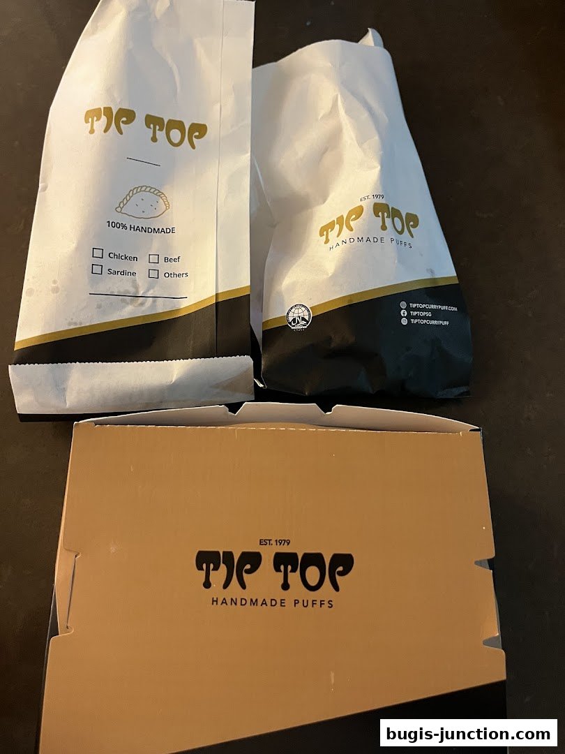 Two white paper bags and a cardboard box with the Tip Top logo and 'Handmade Puffs' text.