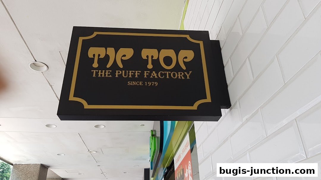 A black sign with gold lettering for 'Tip Top The Puff Factory Since 1979'.