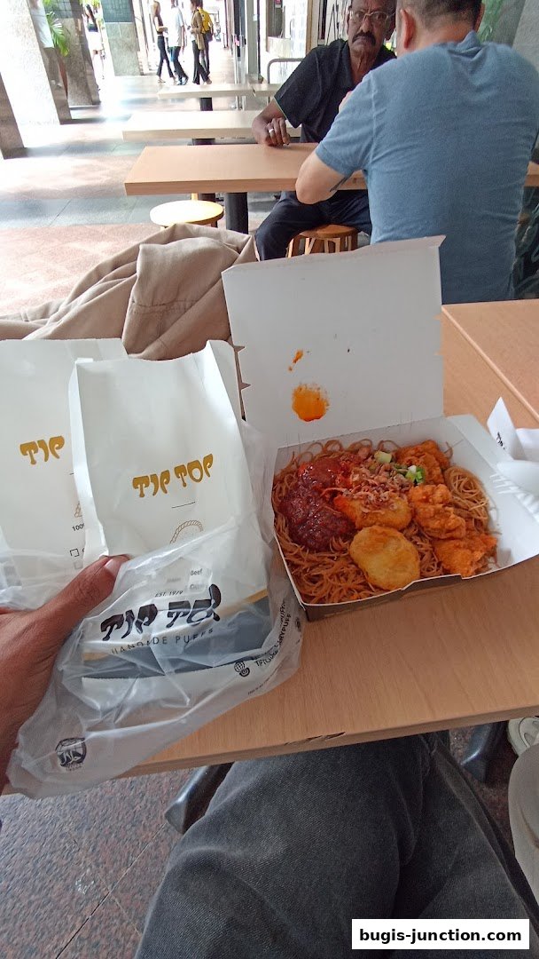 A person holding Tip Top Curry Puff bags with a meal box on a table.