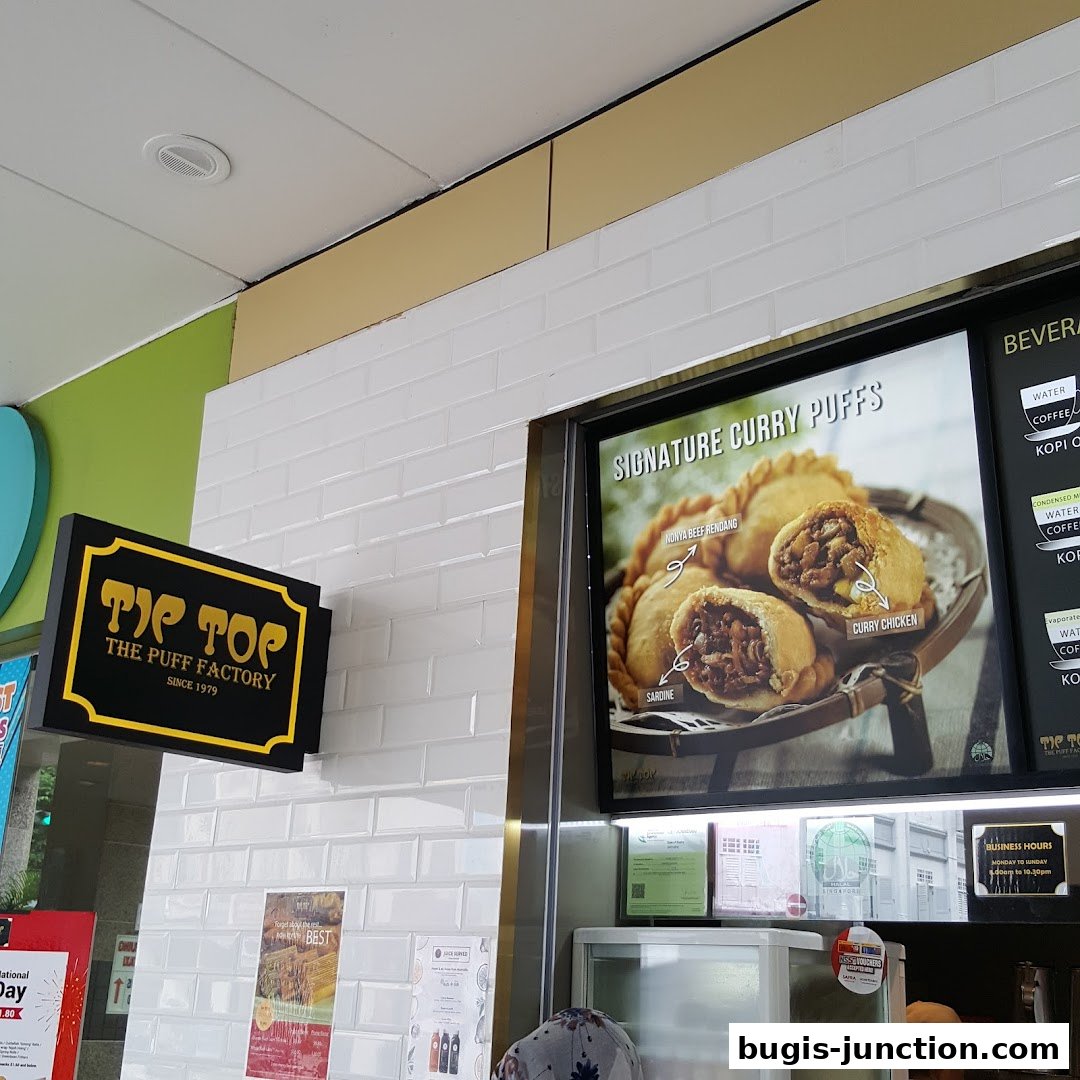 A sign for Tip Top Curry Puff with a display of signature curry puffs and beverages.