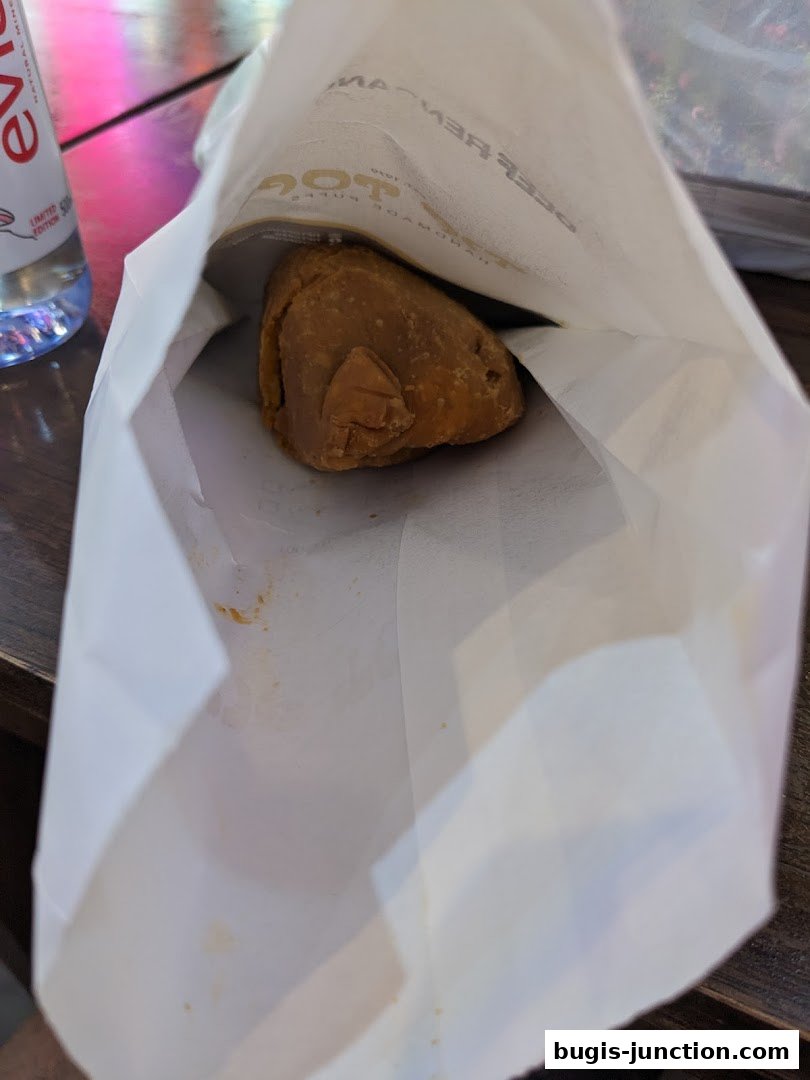 A single curry puff sits inside a white paper bag with the shop's logo visible.