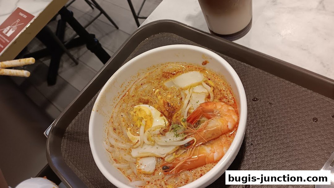 A bowl of Laksa with prawns, egg, and fish cakes, served on a tray.