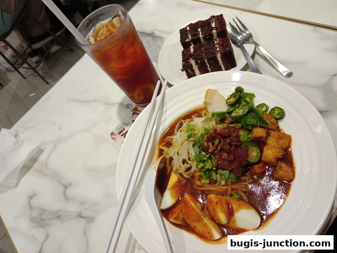 A plate of noodles with egg and chili, a slice of chocolate cake, and a glass of iced tea.