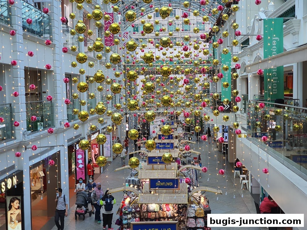 A shopping mall interior decorated with numerous gold and pink spherical ornaments and fairy lights.