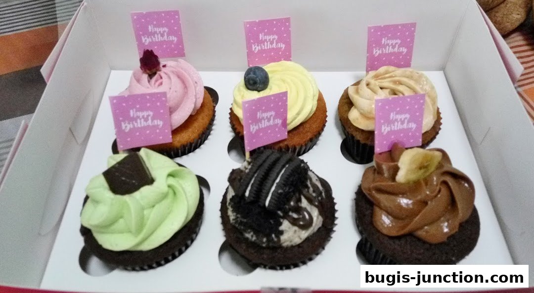 A box of six assorted cupcakes, each decorated with frosting and a 'Happy Birthday' flag.