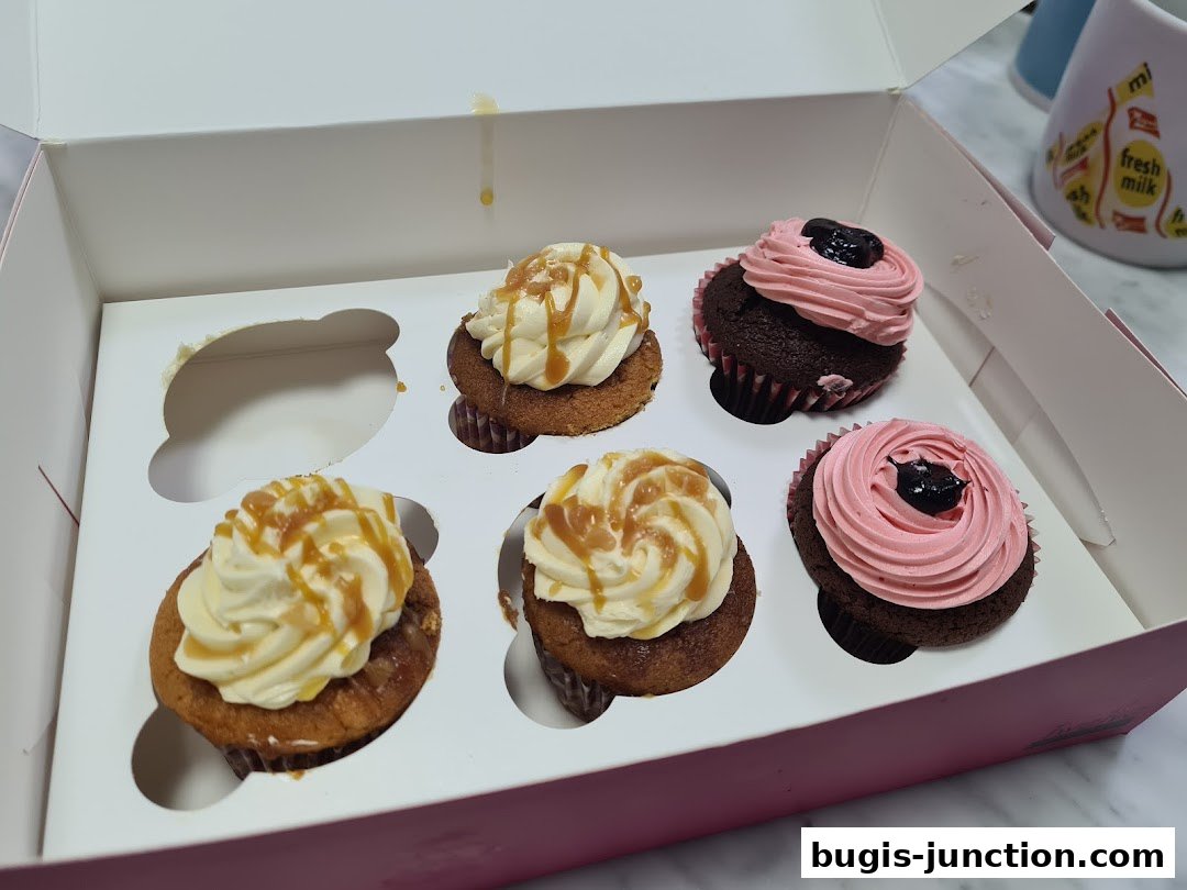 A box of six assorted cupcakes, some with caramel drizzle and others with pink frosting and a dark topping.