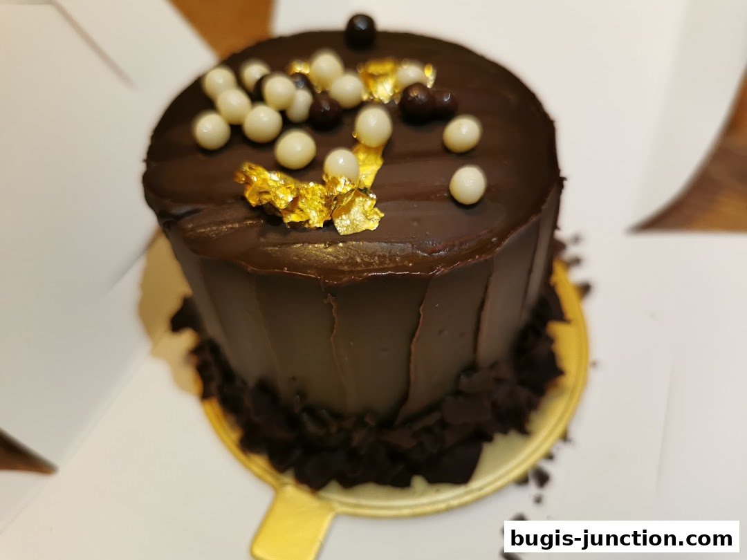 A decadent chocolate cake adorned with white chocolate balls and gold leaf.