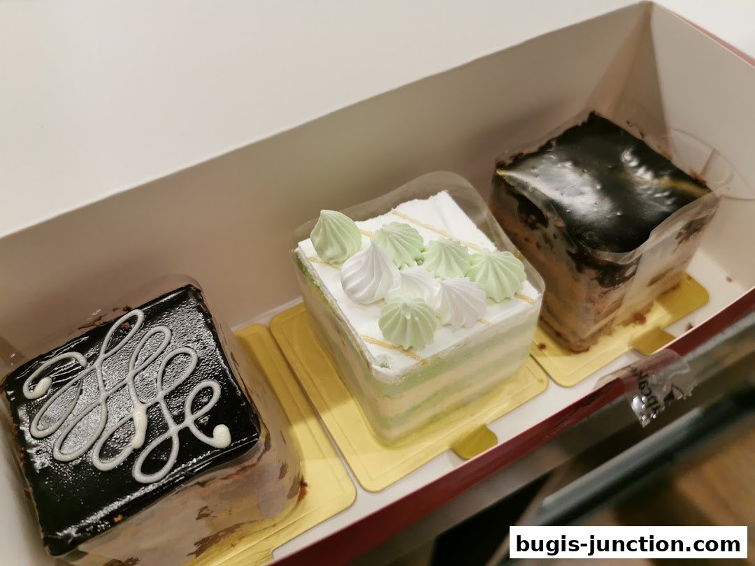 A box containing three delicious-looking individual cakes, two chocolate and one layered green and white.