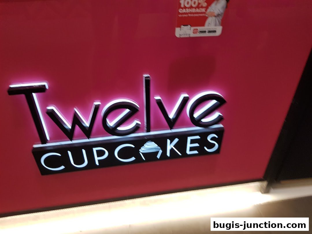 The illuminated logo of "Twelve Cupcakes" is displayed on a vibrant pink wall.
