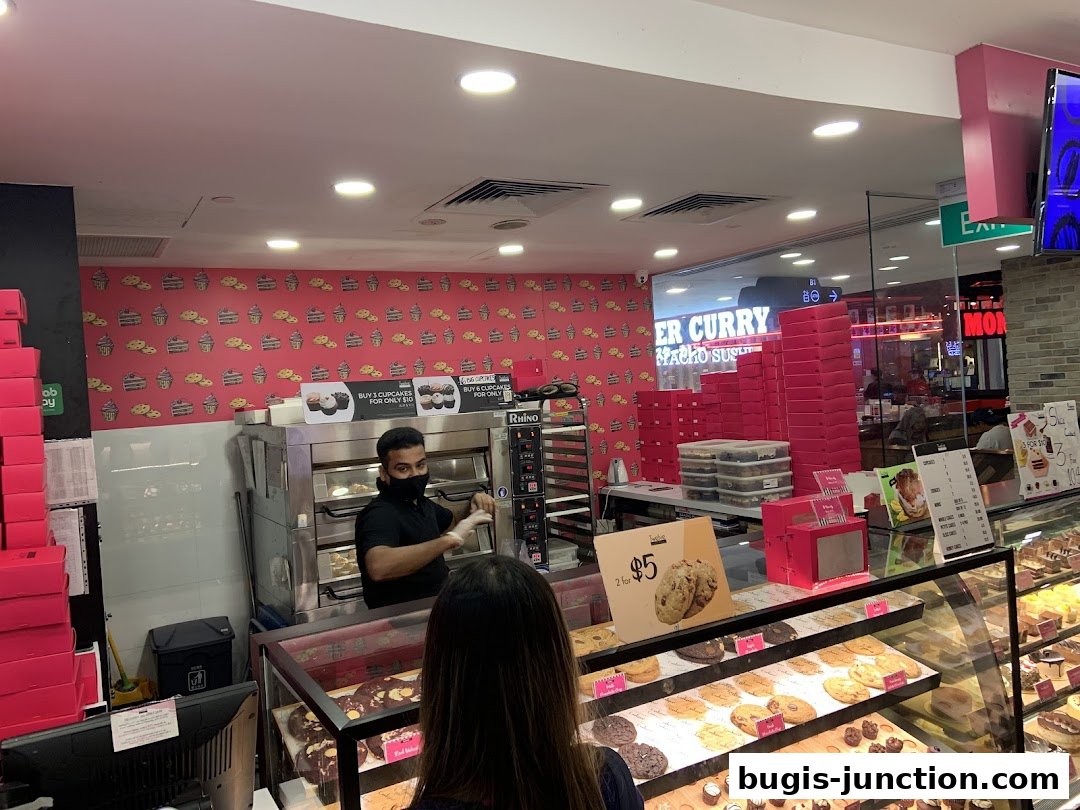 A baker serves customers at Twelve Cupcakes, with displays of cookies and cupcakes.