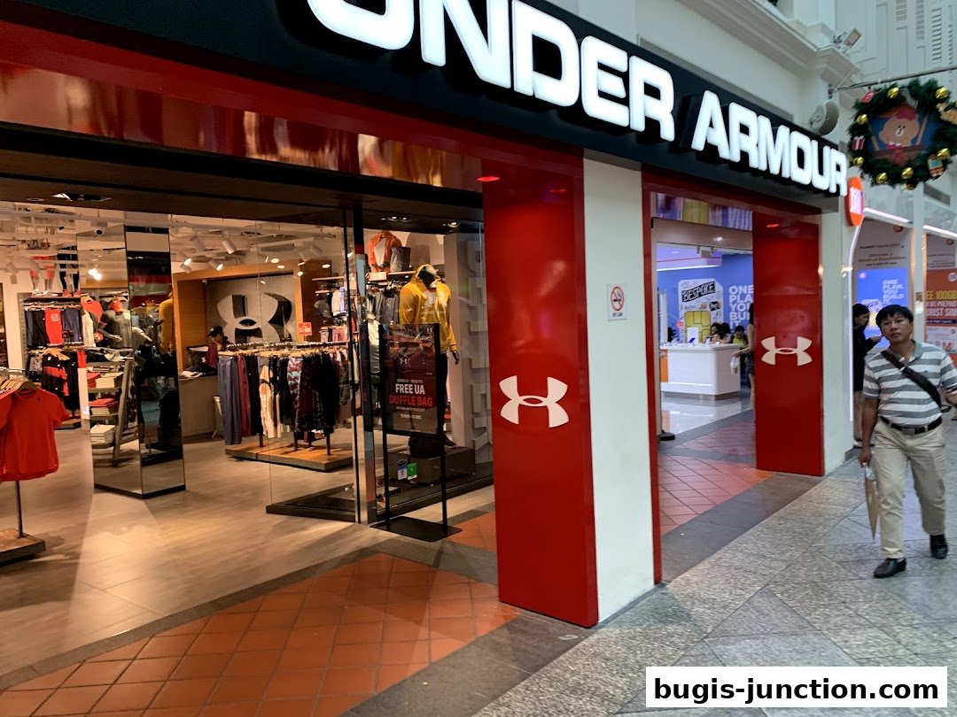 The entrance of an Under Armour store with sportswear displayed inside and a man walking past.