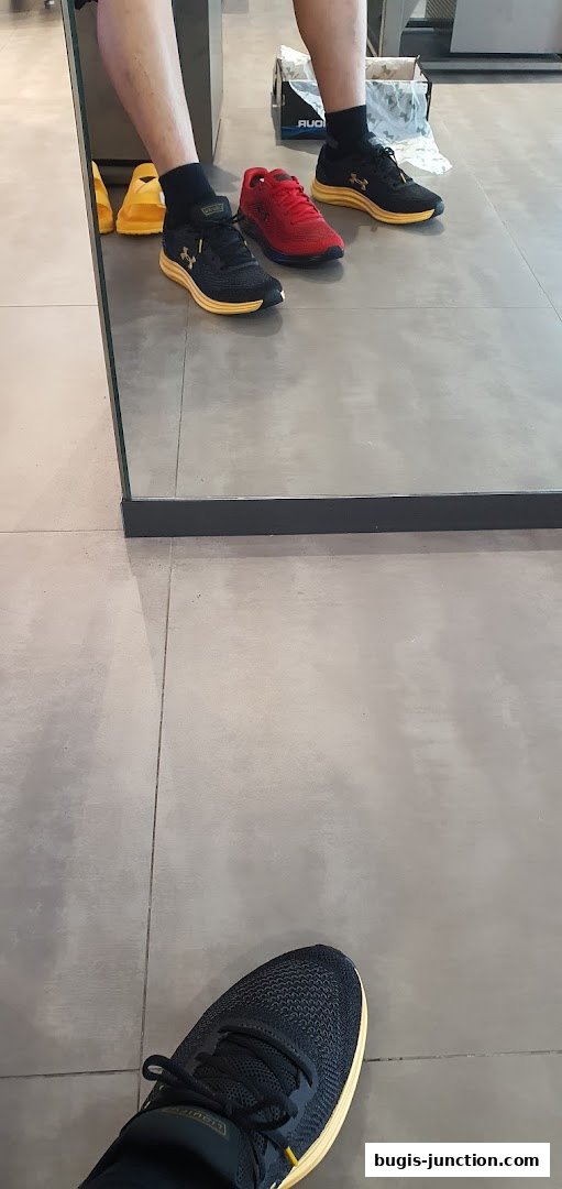 A person trying on Under Armour shoes in a store, with multiple pairs displayed.