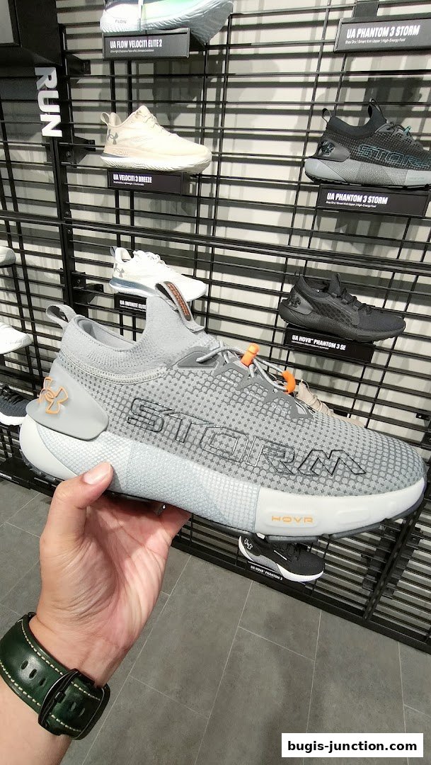 A hand holds a grey Under Armour running shoe with 'STORM' text on display.