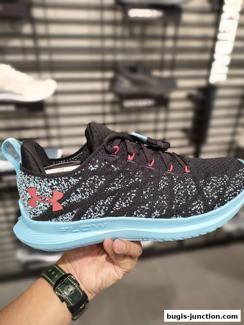 A hand holds a black and blue Under Armour running shoe with a light blue sole.