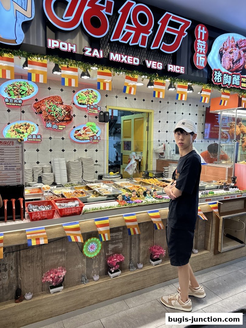A young man stands in front of a food stall displaying various dishes and menu items.