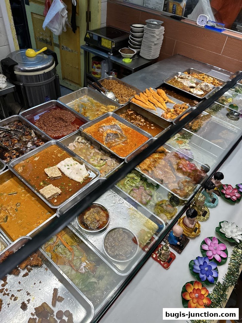 A display of various cooked dishes in metal trays, with decorative items on the side.