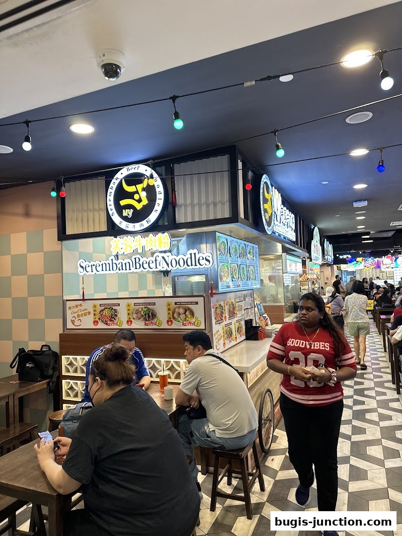 People dining at Seremban Beef Noodles stall in a food court.