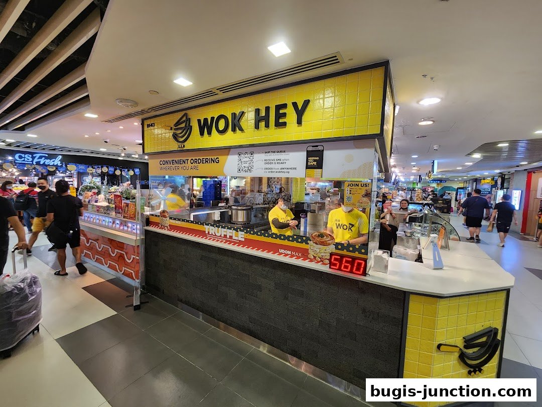 A Wok Hey food stall with staff serving customers and a digital display showing '560'.
