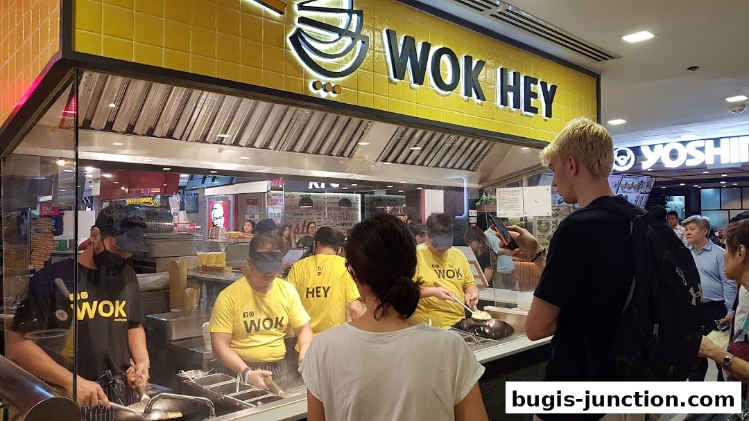 Wok Hey staff preparing food behind a counter with customers in front.