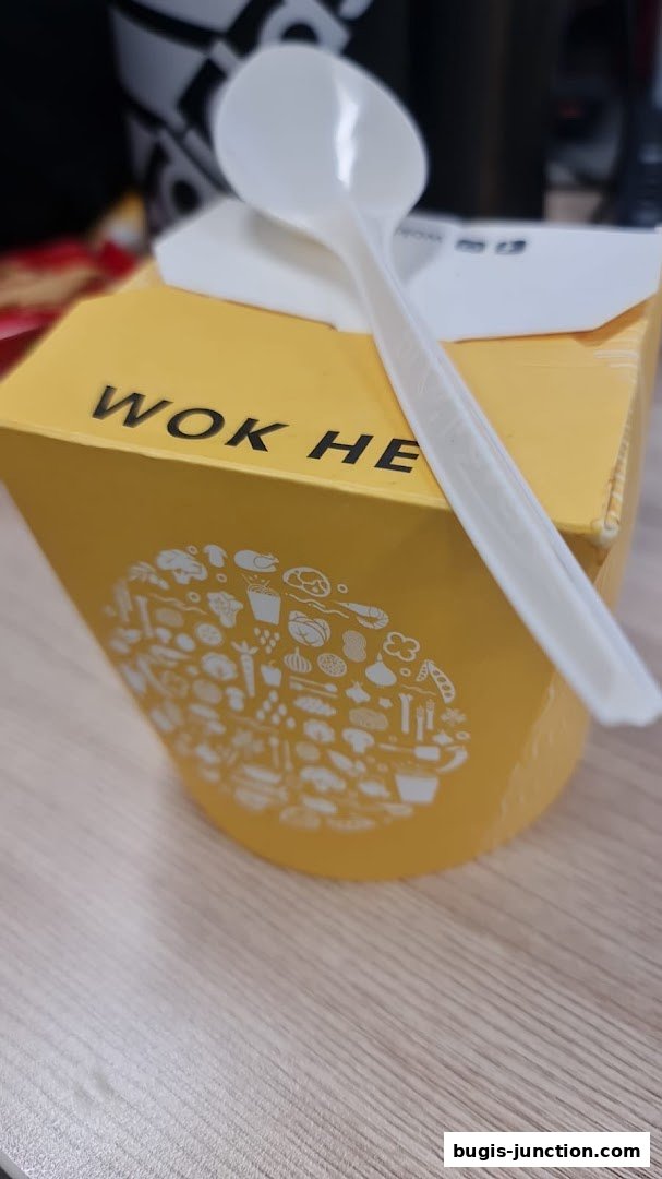 A yellow WOK HEY takeaway box with a white plastic spoon on top.