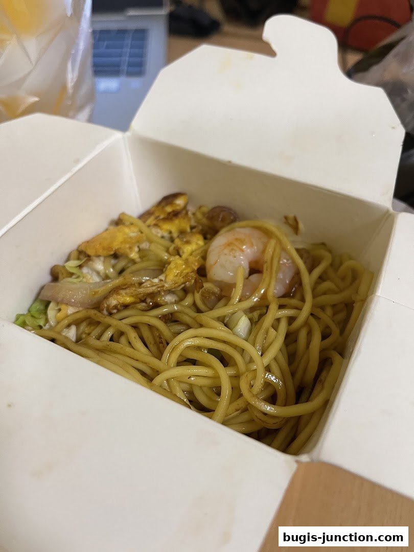 A close-up of a takeaway box filled with noodles, shrimp, and scrambled eggs.