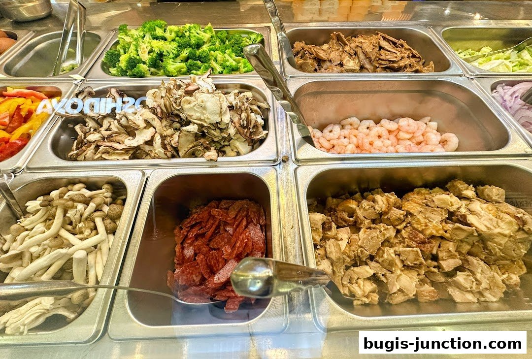 A variety of fresh ingredients like broccoli, mushrooms, shrimp, and meats are displayed in metal trays.