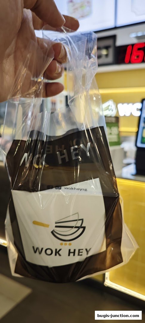 A hand holds a Wok Hey takeaway bag with the restaurant's logo and name.