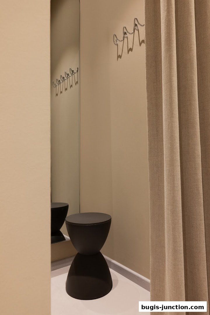 A clean and modern fitting room with a mirror, stool, and curtain.