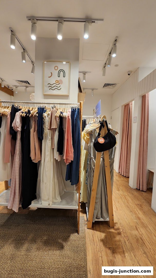 Interior view of a clothing store with racks of dresses and a black handbag on display.