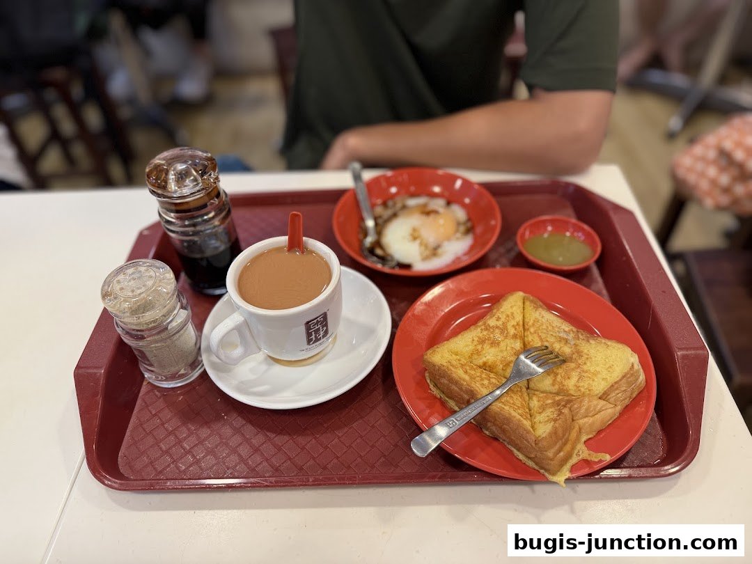 A tray of traditional Singaporean breakfast with kaya toast, soft-boiled eggs, and coffee.