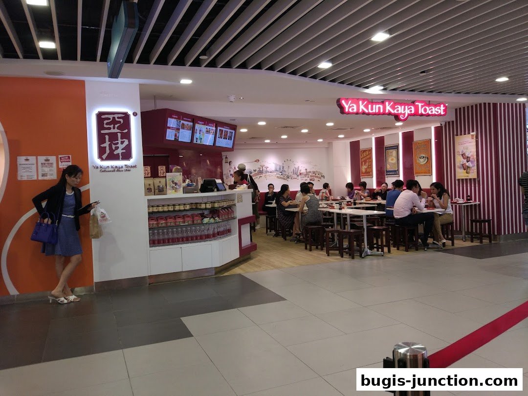 Interior view of Ya Kun Kaya Toast with customers dining and a woman standing near the counter.