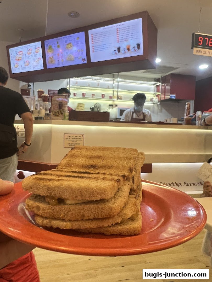 A close-up of stacked kaya toast on a red plate in front of a Ya Kun Kaya Toast counter.