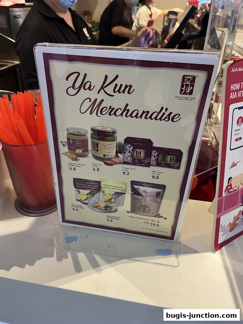 A sign displays Ya Kun Kaya Toast merchandise including jars of kaya, cookies, and coffee powder.