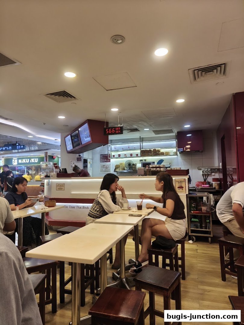 Two women are sitting at tables in a cafe, with other patrons visible.