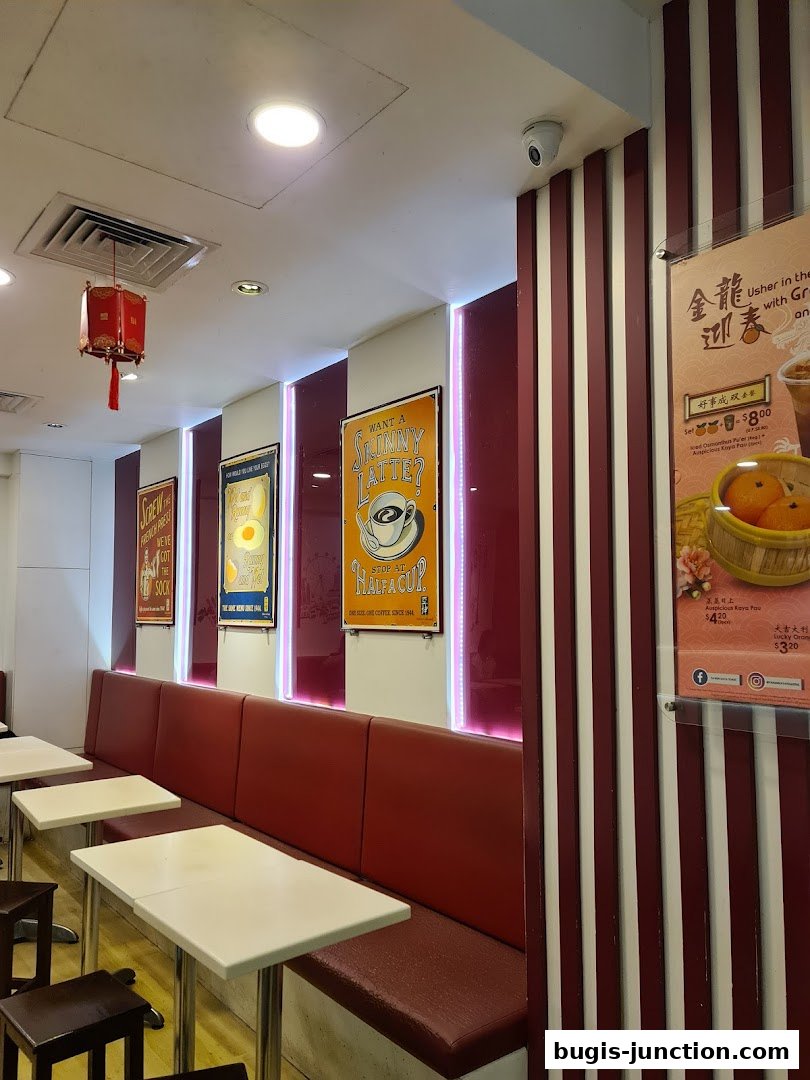 Interior of Ya Kun Kaya Toast with red booth seating, tables, and promotional posters on the wall.