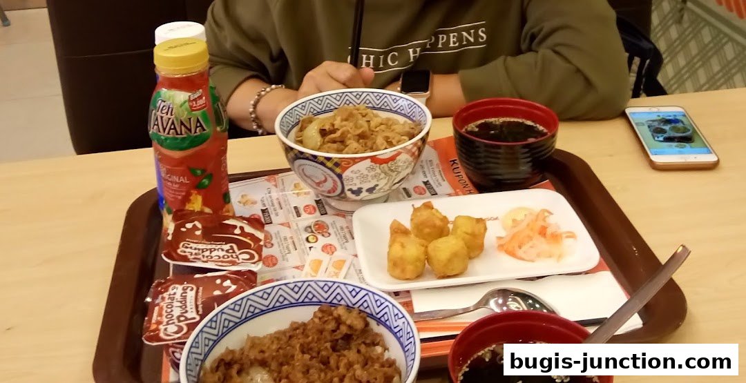 A tray of Yoshinoya food including beef bowls, fried items, and dessert.