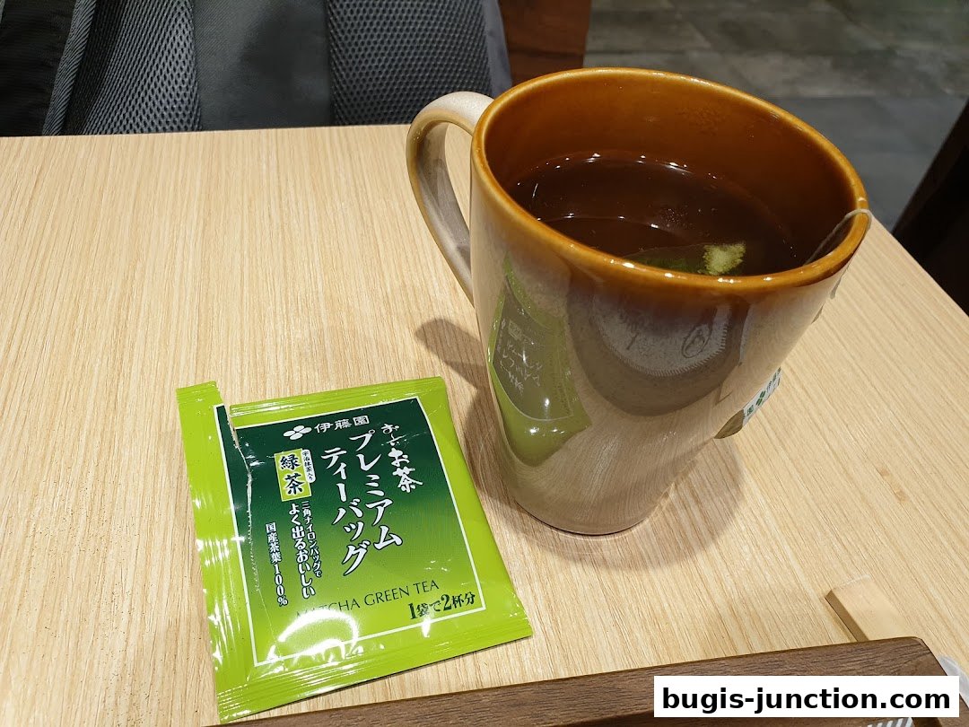 A cup of green tea with a premium matcha green tea bag on a wooden table.