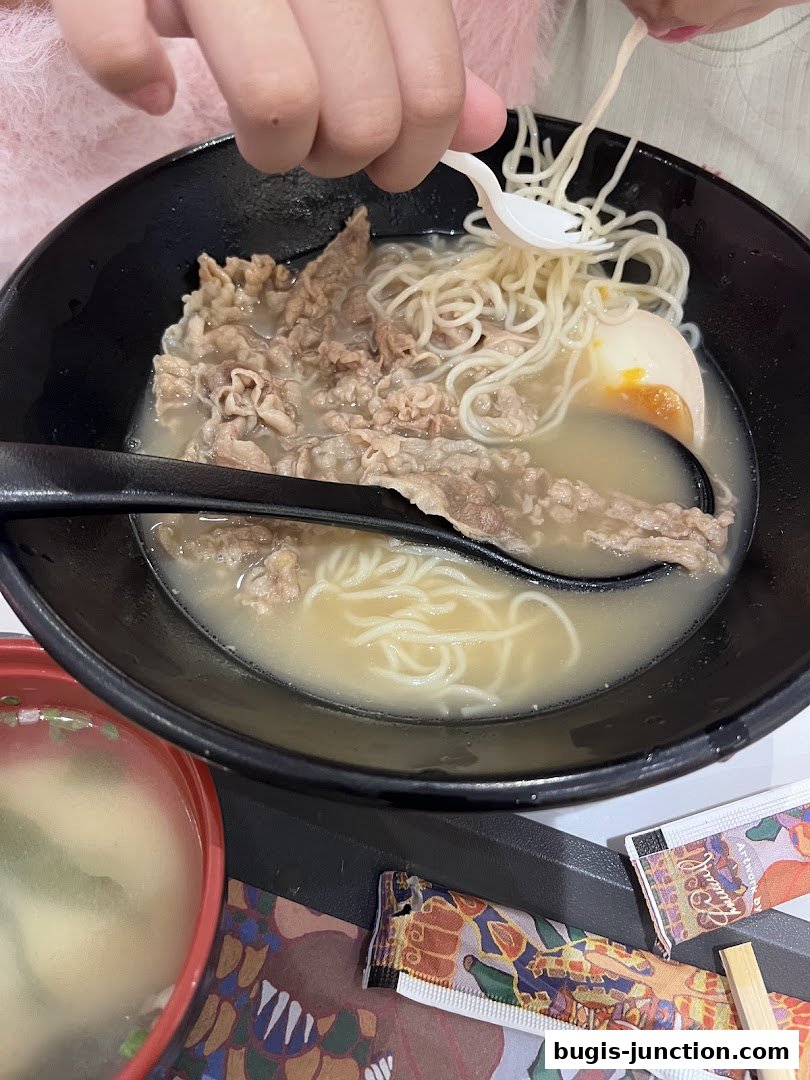 A close-up of a delicious bowl of beef ramen with a soft-boiled egg and a side of miso soup.