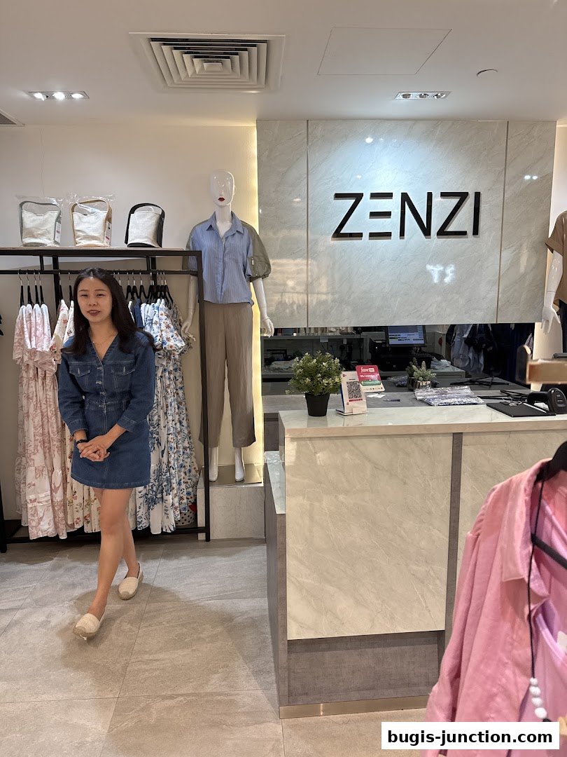 A woman stands in a clothing store with racks of dresses and a mannequin.